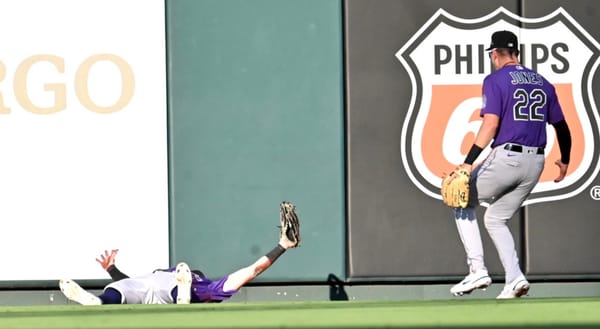 Brenton Doyle lies on the grass in center field, his mitt raised in triumph as Nolan Jones runs to congratulate him. Both are