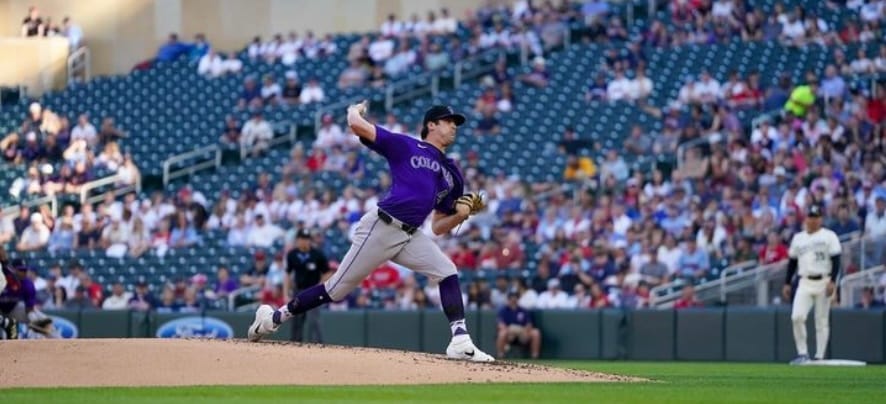 Quantrill is in the windup. He’s wearing a purple jersey and gray pants.