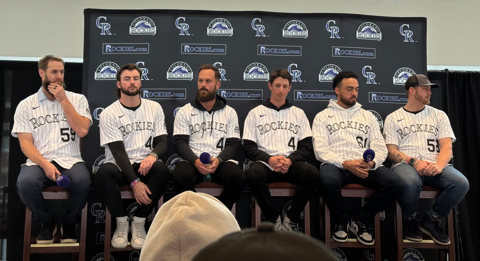 The pitchers sit on tall chairs. They are wearing purple pinstriped jerseys.