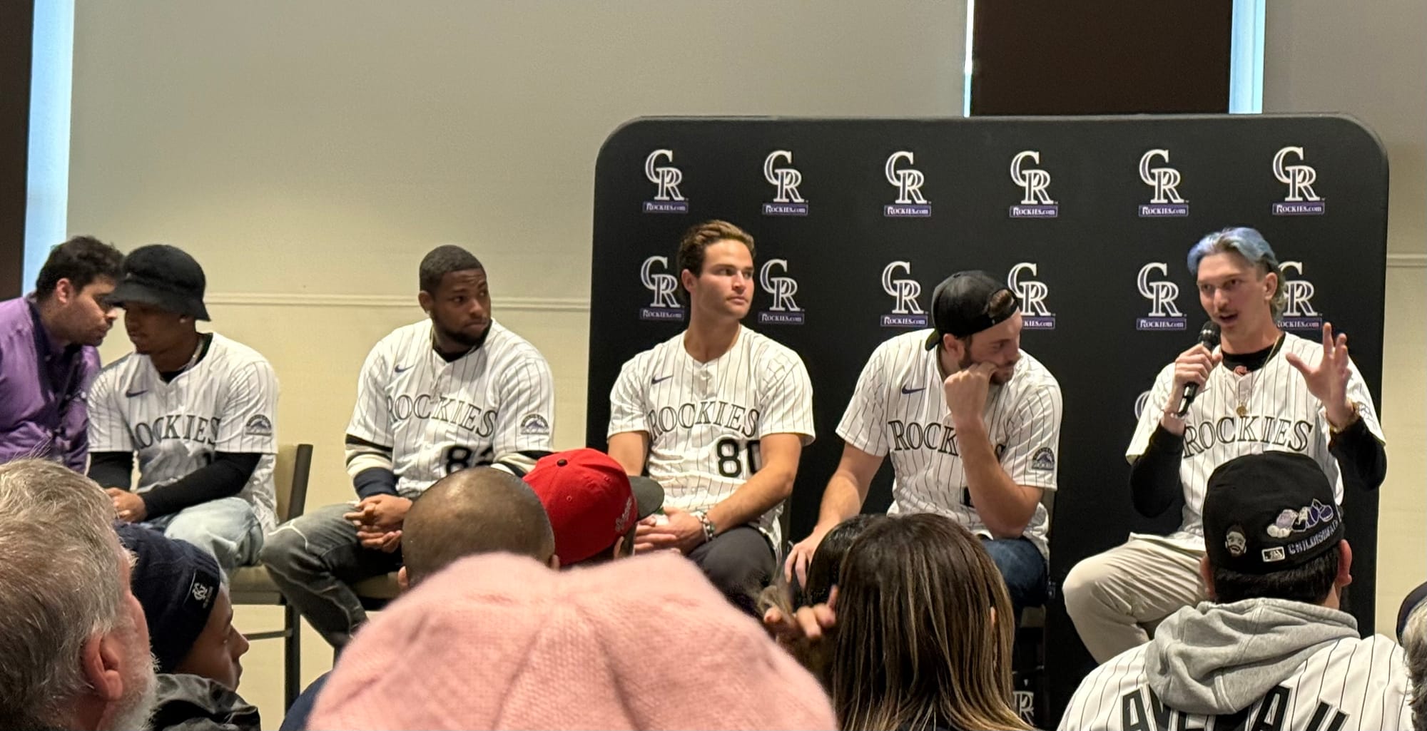 The prospects are seated on tall chair and wear purple pinstriped jerseys. Veen has blue hair. 