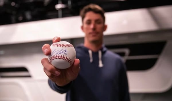 Herget, wearing a blue hoodie, holds a signed baseball. The ball is clear; Herget’s image is blurry.