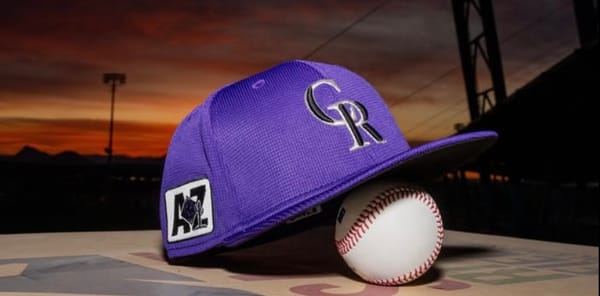 A purple Rockies cap rests on a baseball with the Arizona skyline in the background.